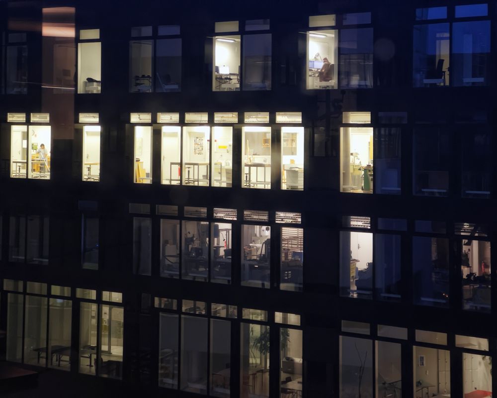 Office building exterior with lit windows at night, showing various workspaces.