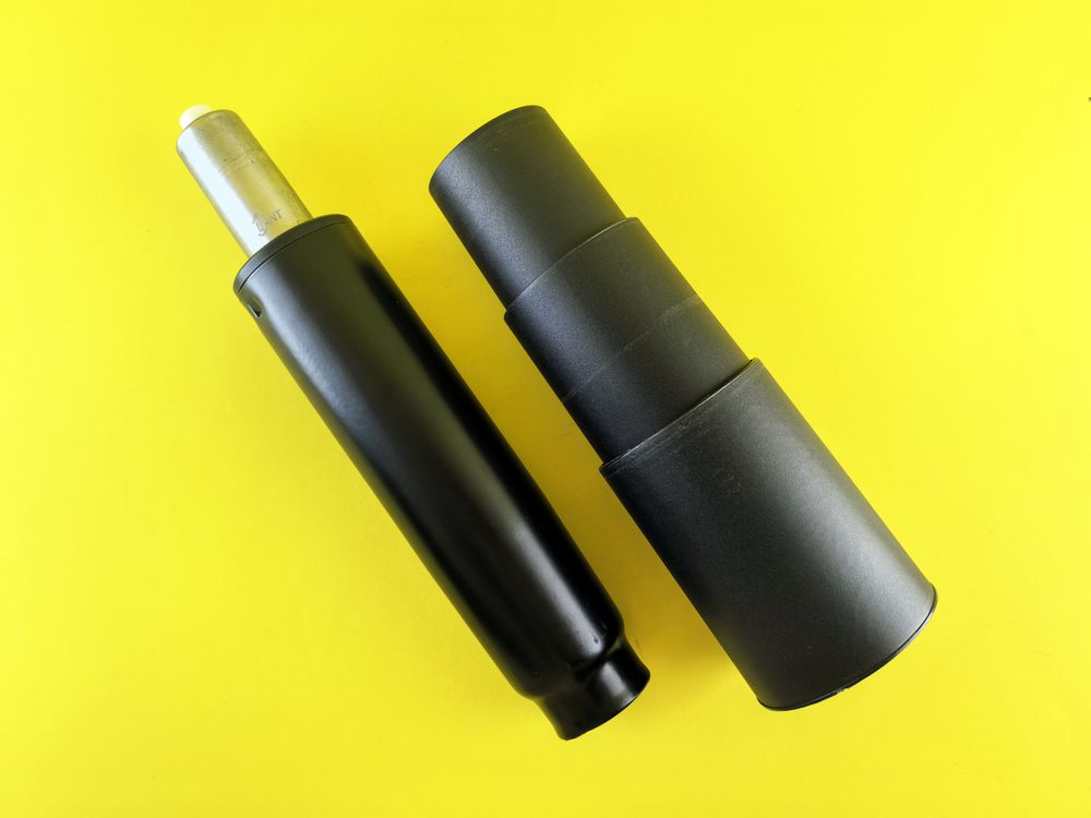 Two black gas lift cylinders for office chairs displayed on a bright yellow background.