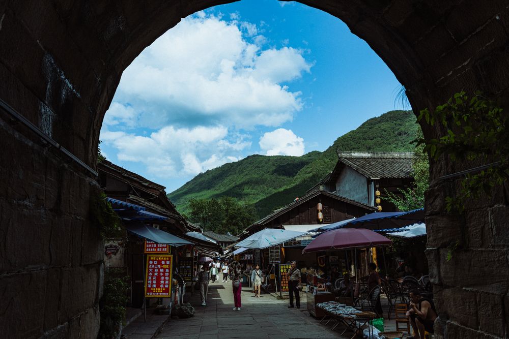 Explore a bustling traditional market nestled in a quaint alleyway framed by striking mountains.