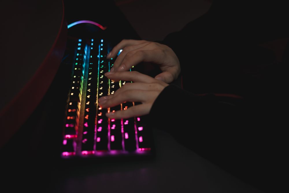 Close-up of hands typing on a colorful RGB backlit mechanical keyboard in a dimly lit environment